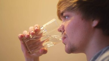 Genç susuz bir adam filtrelenmiş temiz su içiyor. Kavram. Şeffaf cam ve içme suyu, su ve sağlık konseptini tutan susamış adamın yan görüntüsü.