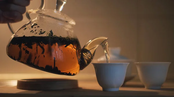 Close up of teapot with black chinese tea, gaiwan and pialas on the wooden table. Концепция. Женская рука разглядывает горячий напиток в маленькие белые чашки. — стоковое фото