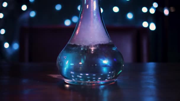 Kamera entfernt sich von der Glasflaschenvase für eine Wasserpfeife. Medien. Transparente Flasche mit Wasser auf dunklem Raumhintergrund, dekoriert mit blauen Lampen.