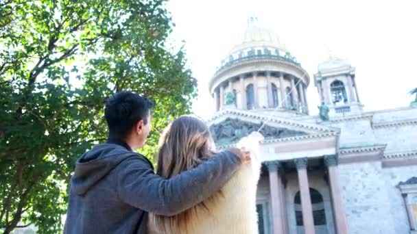 Visão traseira de um casal feliz de pé e discutindo templo incrível perto de arbusto verde. Conceito. Homem abraçando mulher, olhando para bela Catedral e apontando um dedo. — Vídeo de Stock