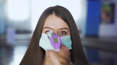 Maskeli kadın AVM 'de sıcaklığı kontrol ediliyor. Medya. Sinema ve alışveriş merkezlerini ziyaret edenler temas olmayan termometre kullanılarak sıcaklık için kontrol edilirler.
