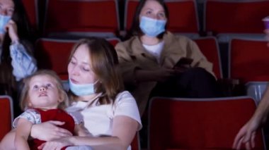 Sinemada maskeli bir aile. Medya. Çocuklu genç bir aile koronavirüs salgını sırasında sinemada çizgi film izlemeye gelmiş. Sinemada maskeli bir aile.