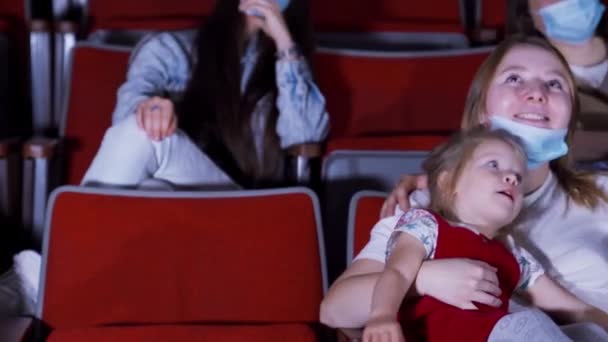 Família mascarada no cinema. Mídia. Jovem bela família assistindo desenhos animados no cinema durante a pandemia. Família com criança usando máscaras no cinema — Vídeo de Stock