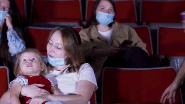 Familia con máscaras en el cine. Medios. Una familia joven con niños vino a ver dibujos animados en el cine durante la pandemia de coronavirus. Familia en el cine sentado en máscaras médicas — Vídeos de Stock