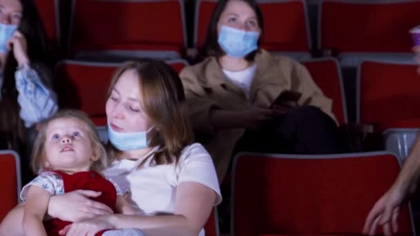 Famille masquée au cinéma. Les médias. Une jeune famille avec enfant est venue voir des dessins animés au cinéma pendant la pandémie de coronavirus. Famille au cinéma assis dans des masques médicaux — Video