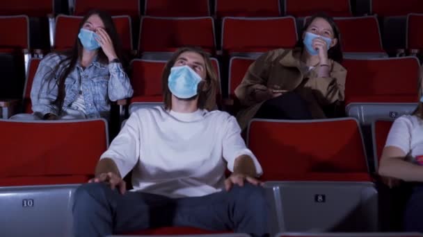 As pessoas mascaradas vêem filmes engraçados. Mídia. Pessoas em máscaras médicas sentam-se no cinema e riem enquanto assistem ao filme. Abertura de cinemas durante o coronavírus pandêmico — Vídeo de Stock