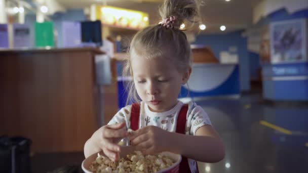 Mała dziewczynka je popcorn w kinie. Media. Słodka dziewczyna jedząca popcorn w poczekalni w kinie. Pretty girl słodkie jedzenie popcorn — Wideo stockowe