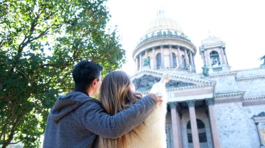 Yeşil çalı yakınlarındaki muhteşem tapınağı tartışan mutlu bir çiftin arka görüntüsü. Kavram. Erkek kadına sarılıyor, güzel katedrale bakıyor ve parmağıyla işaret ediyor..