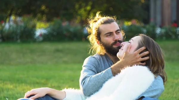 Amar abraços casal e beijos enquanto sentado na grama no parque. Conceito. Doce e belo homem e mulher desfrutando e passando tempo juntos. — Fotografia de Stock