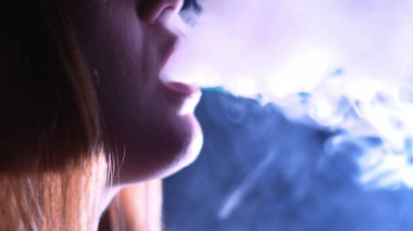 Bir gece kulübünün karanlık odasında sigara içen kadın. Medya. Şehvetli bir kadının dudaklarıyla nargile tübüne dokunuşunu ve beyaz dumanını yakından izleyin..