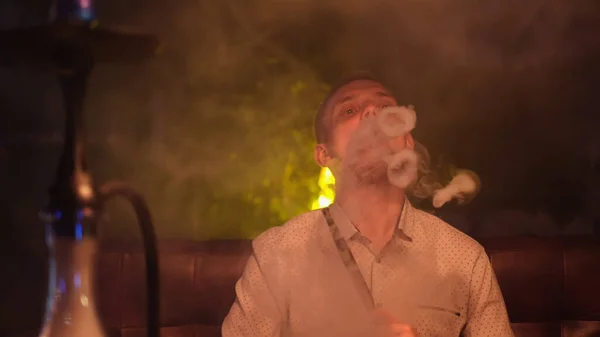 Portret człowieka palącego tradycyjną fajkę hookah i robiącego chmury dymne w formie pierścieni. Media. Człowiek wydychający dym w kawiarni Hookah lub barze. — Zdjęcie stockowe