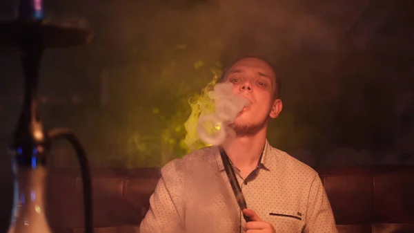 Portret van de mens die traditionele hookah pijp rookt en rookwolken maakt in de vorm van ringen. De media. Man die rook uitademt in hookah café of lounge bar. — Stockfoto