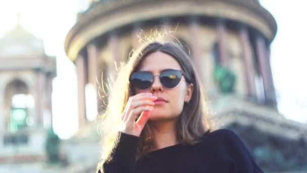 Verbazingwekkende jonge vrouw die zwarte glazen afdoet die haar haar aanraken bij winderig zomerweer. De media. Buiten portret van schattig meisje met vliegend haar glimlachen en poseren in de voorkant van de camera in de stad op oud — Stockvideo