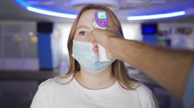 Maskeli kadın AVM 'de sıcaklığı kontrol ediliyor. Medya. Sinema ve alışveriş merkezlerini ziyaret edenler temas olmayan termometre kullanılarak sıcaklık için kontrol edilirler.