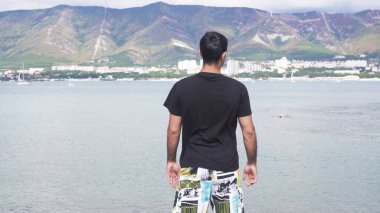 Deniz ve dağların arka planında beyaz bir adamın dikiz görüntüsü. Medya. Genç adam dağlarla birlikte denizde tatilde. Denizin ve dağların ötesindeki güzel insan manzarası