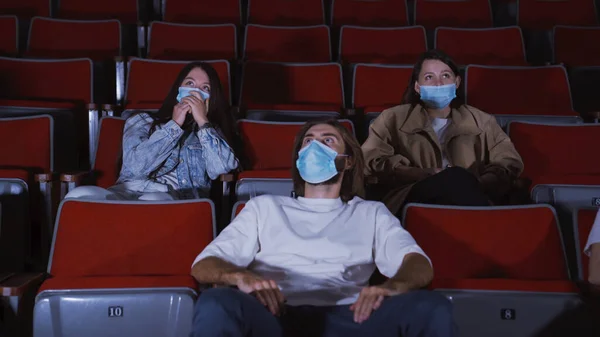 People in movie theater watch scary movie. Media. Watching movies in medical masks during coronavirus pandemic. People in masks watch scary movies