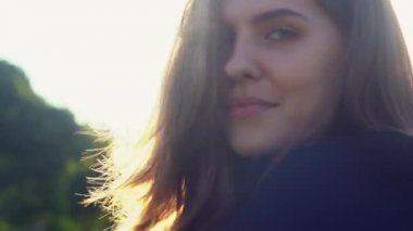 Saçları rüzgarda uçuşan, güneşe karşı çarpıcı bir kız yüzü. Medya. Dışarıda poz veren, kameraya gülümseyen ve saçlarına dokunan genç bir kadın..