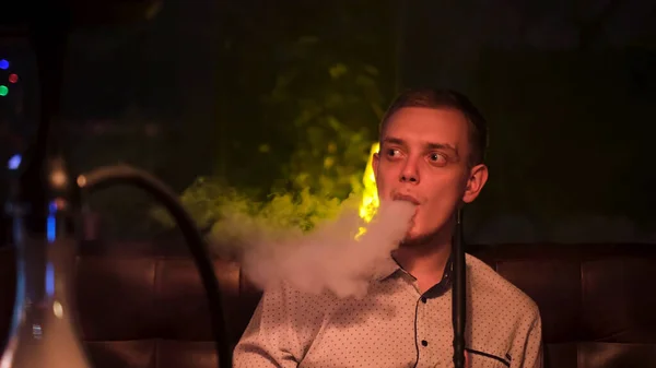 O jovem moderno na moda fuma narguilé no bar à noite. Mídia. Loiro segurando tubo de shisha, conceito de fumar um narguilé e se divertir. — Fotografia de Stock