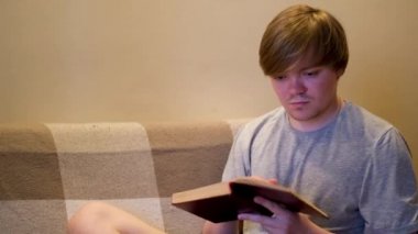 Eski bir kitabın sayfasını çevirip içerideki koltukta oturan bir adamın portresi. Kavram. Beyaz erkek okuyucu evde edebiyat, okuma, hobi ve yaşam tarzı kavramından keyif alıyor..