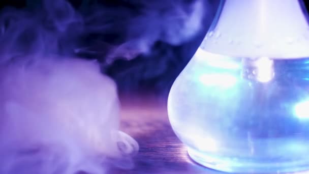 Primer plano de vidrio frasco transparente de narguile sobre la mesa con una nube de humo. Medios. Frasco Shisha bajo la lámpara azul de pie sobre una mesa de madera. — Vídeo de stock