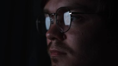 İşadamı, programcı ya da programcı gece geç saatlere kadar dizüstü bilgisayarla çalışıyor. Kavram. Gözlüklerine yansıyan bilgisayar ekranıyla karanlıkta düşünceli bir adam..
