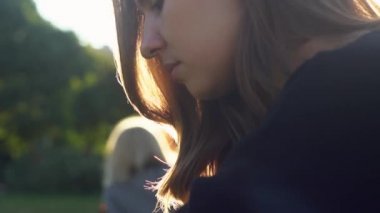 Günbatımı ve güneş ışığının arka planında genç bir kadın var. Medya. Siyah örgü kazaklı çekici bir kız kameraya bakıyor, saçları rüzgarda uçuşurken gülümsüyor..