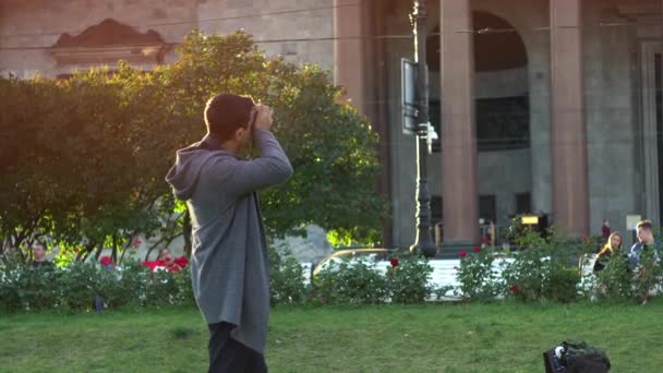 Visões turísticas de fotografia e pontos de referência. Mídia. Jovem viajante homem tirar fotos em sua câmera no parque da cidade, no fundo do enorme edifício com pilares de granito. — Vídeo de Stock