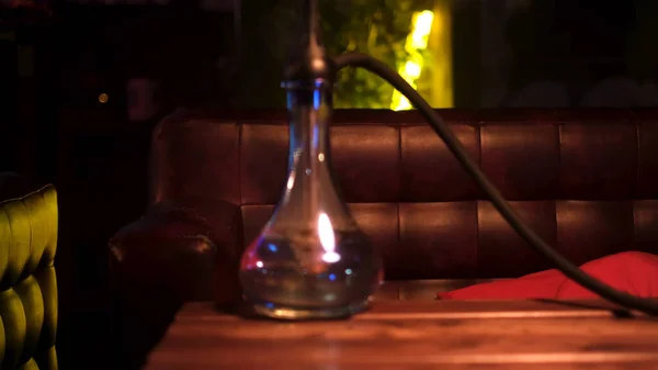 Close-up van handgemaakte hookah geplaatst op een houten tafel in een hookah bar. De media. Gezellige sfeer en de shisha glazen kolf op leren bank en groene neon lamp achtergrond. — Stockfoto