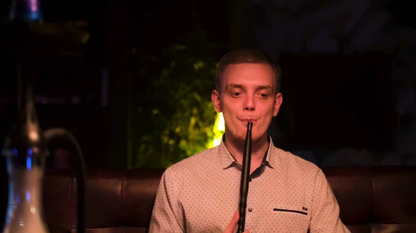 Молодий хлопець курить кальян в нічному барі і виглядає сумно, концепція самотності. Медіа. Блондинка з поганою звичкою, альтернатива тютюну . — стокове фото