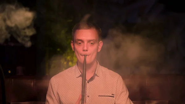 Ο νεαρός καπνίζει ναργιλέ μόνος στο νυχτερινό μπαρ και δείχνει λυπημένος, με την έννοια της μοναξιάς. Μέσα ενημέρωσης. Ξανθός άνδρας με κακή συνήθεια, μια εναλλακτική λύση για τον καπνό. — Φωτογραφία Αρχείου
