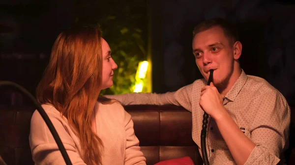Man and woman on a date at hookah bar smoking and chatting. Media. Male smoker listen to his girlfriend carefully while smoking shisha under the dim light. — Stock Photo, Image