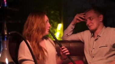 Gece kulübünde Shisha içerken mutlu çift etkileşimi. Medya. Genç bir adam ve bir kadın birbirleriyle konuşuyor, eğleniyorlar, kız duman üflüyor, aşk kavramı..