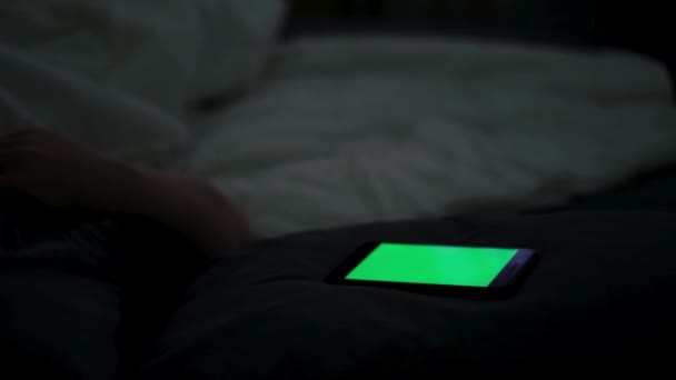 Großaufnahme eines digitalen Handys mit grünem Bildschirm und eines Mannes im Bett. Konzept. Schläfriger Mann, der sein Smartphone benutzt und versucht zu schlafen, Konzept der Telefonsucht und Schlaflosigkeit. — Stockvideo