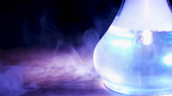 Närbild av glas transparent kolv av hookah på bordet med ett moln av rök. Media. Shisha-kolven under den blå lampan som står på ett träbord. — Stockfoto