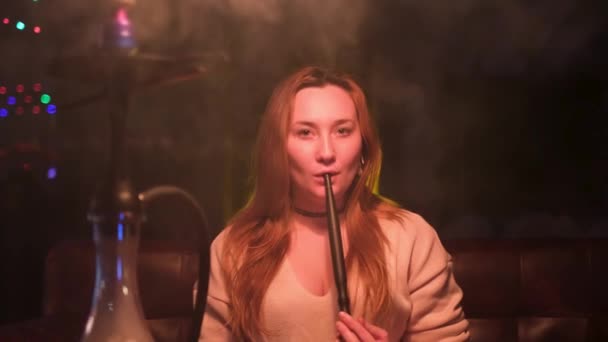 Hermosa mujer joven sexy con maquillaje natural vapeo en discoteca. Medios. Mujer exhalando humo en el bar y mirando directamente a la cámara. — Vídeo de stock