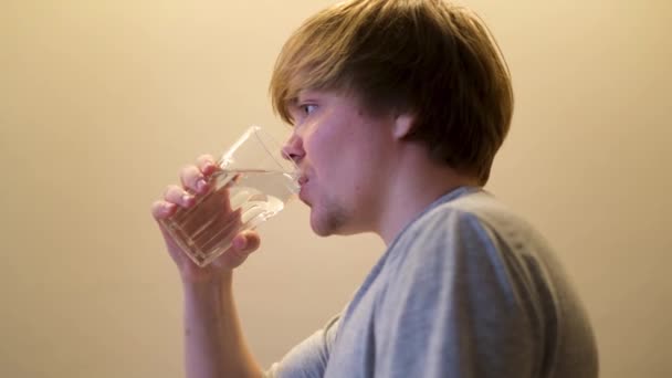 Seitenansicht eines blonden kaukasischen Mannes, der klares Wasser trinkt. Konzept. Durstiger junger Kerl hält Glas mit transparentem Wasser und trinkt isoliert auf gelbem Wandhintergrund. — Stockvideo