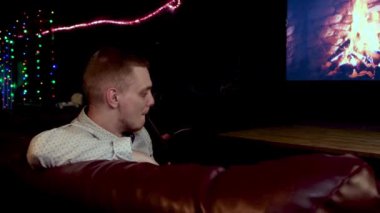 Genç adam şöminenin yanında nargile içerken dinleniyor. Medya. Şöminenin yanında sigara içen bir adam TV ekranında resmedilmiş..