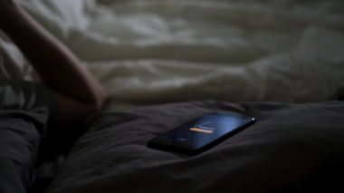 Dijital cep telefonu ekranındaki çalar saati kapat ve bir adamı yatakta uyandır. Kavram. Uykulu adam çalar saati kapatıp evdeki rahat yatağında uyumaya devam ediyor..