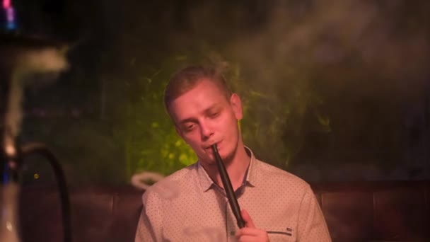 Jeune homme fume narguilé seul au bar de nuit et l'air triste, concept de solitude. Les médias. Homme blond avec une mauvaise habitude, une alternative au tabac. — Video
