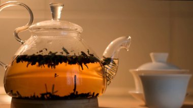 Dolu bir çaydanlık ve bej duvar arkasında izole edilmiş küçük beyaz bir Çin bardağı. Kavram. Geleneksel gaiwan ve fincanın yanında cam çaydanlıkta nefis bir çay..