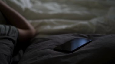 Uyuyan adamı ve telefonunu yatağın üzerine koy. Kavram. Geceleri akıllı telefonuyla uyuyan bir adam evdeki battaniyenin üzerinde yatıyor..
