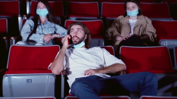 El tipo habla por teléfono y molesta a la gente en un cine. Medios. Mujer joven pidiendo que se detenga el otro hombre hablando en el teléfono móvil mientras ve la película en el cine. — Vídeo de stock