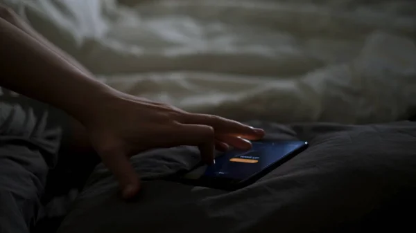 Close up of sleeping man being woken up by his phone lying on the bed. Concept. Male hand trying to turn off the alarm clock lying near on a blanket at home early in the morning.