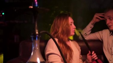 Gece kulübünde Shisha içerken mutlu çift etkileşimi. Medya. Genç bir adam ve bir kadın birbirleriyle konuşuyor, eğleniyorlar, kız duman üflüyor, aşk kavramı..