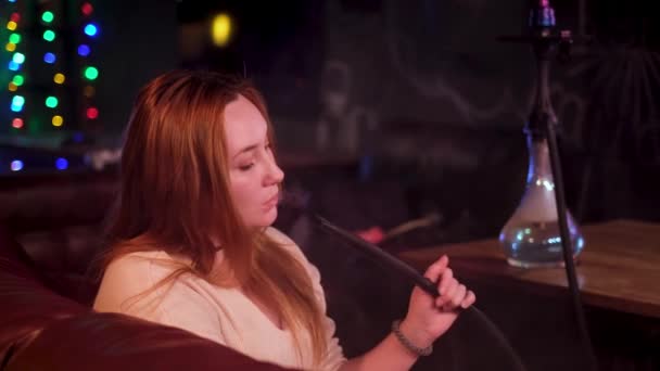 Raucherinnen mit Wasserpfeife auf dunklem Hintergrund im Innenraum eines Nachtclubs. Medien. Plus Size schönes Modell mit einer schlechten Angewohnheit Shisha zu rauchen, Konzept der Freizeit und Entspannung. — Stockvideo