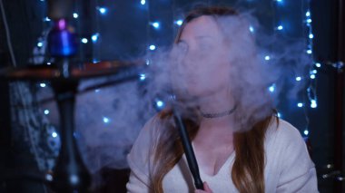 Gece barında nargile tüttüren bej renkli zarif kazaklı çekici bir kız. Medya. Kafkas kadın portresi tüttürüyor ve yalnız vakit geçiriyor..