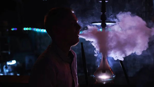 Side view of a man in the dark smoking a hookah. Media. Dark silhouette of a guy relaxing in night club, hookah lifestyle and smoking concept. — Stock Photo, Image