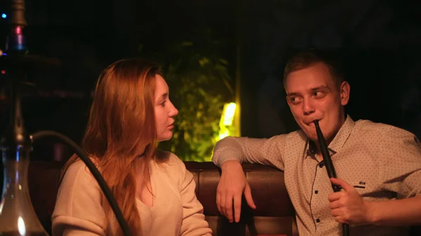 Young loving couple smoking a hookah while sitting in a cafe by the green neon lamp. Media. Young husband and wife enjoying shisha and chatting. — Stock Photo, Image