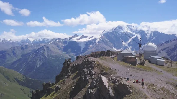 Widok z lotu ptaka Elbrus, widok z lotu ptaka. Klip. Niesamowity widok z góry ludzi spacerujących po wzgórzach otoczony gigantycznymi górami ze śnieżnymi szczytami, koncepcja podróży. — Zdjęcie stockowe