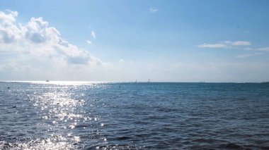 Dalgalanan deniz yüzeyinin mavi bulutlu arka planda parladığı doğal yaz manzarası. Kavram. Güneşli bir yaz gününde, su yüzeyine yansıyan güneş..